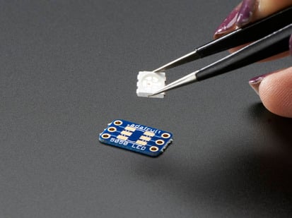 Hand holding 5050 size LED next to breakout board