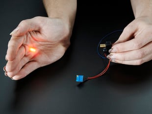 One hand holding laser sensor, other hand blocking the laser output, with a red dot showing on palm.