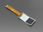 Angled shot of 2.13" monochrome flexible electronic ink display with long ribbon cable. Display is of two white and black blocks.