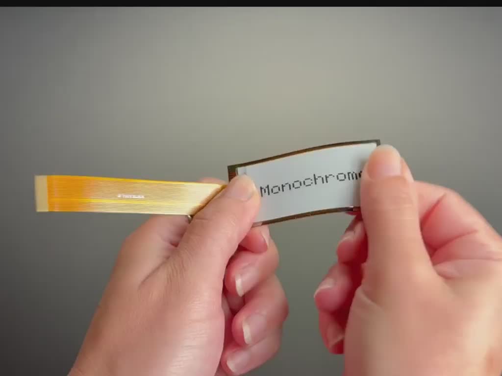 A white hand articulating a flexible electronic ink display module.