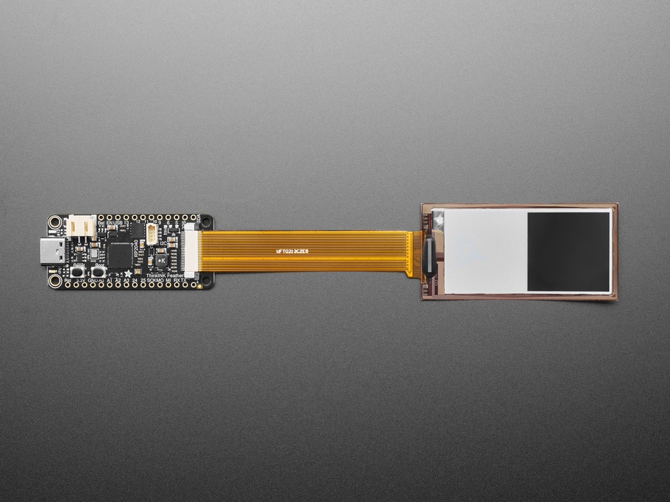 Overhead shot of 2.13" monochrome flexible electronic ink display connected via ribbon cable to a microcontroller. Display is of two white and black blocks.
