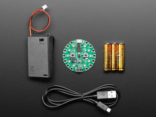 Top-down shot of a round green dev board, a set of three AAA batteries, a microUSB cable, and a AAA battery pack with JST connector.