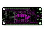 Top-down view of a black/green/purple microcontroller with text that reads "tiny feather".