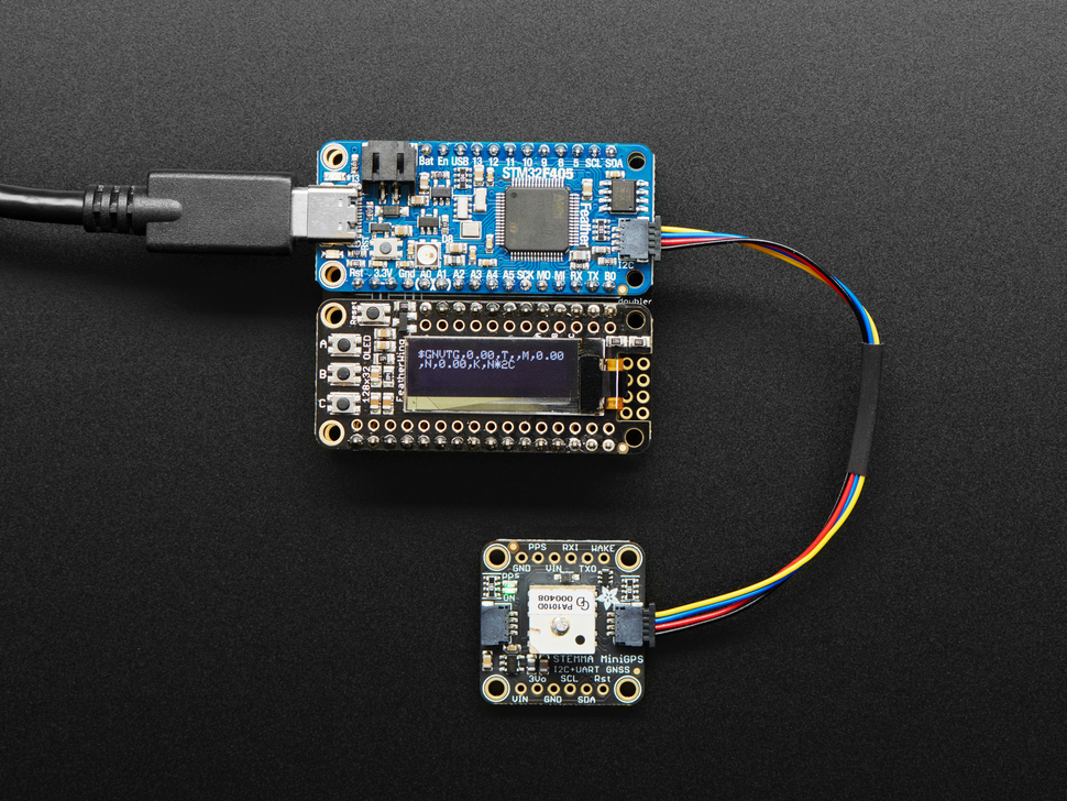 Top view shot of rectangular microcontroller assembled next to an OLED display breakout board can connected to a miniGPS. The OLED displays small white text.