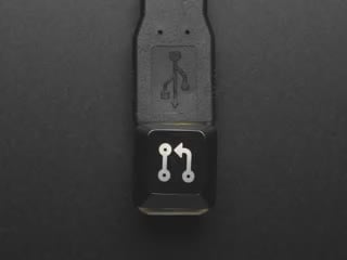 Top view video of black Pull Req keycap connected via USB cable. Various colors emit through the logo.