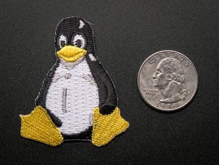 Embroidered badge in the shape of the sitting penguin Linux logo. In black and white, with yellow beak and feet. Shown next to a quarter for scale. 