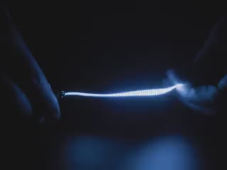 Video of Black hand articulating blue LED filament.
