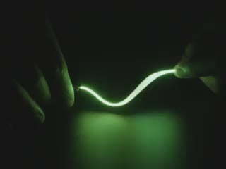 Video of Black hand articulating green LED filament.