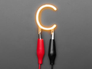 Overhead shot of LED filament in the shape of the letter "C" lit up with alligator clips.