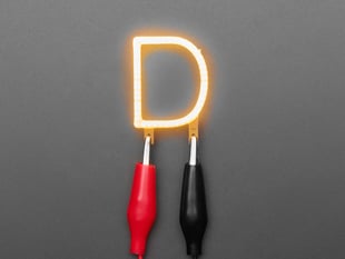 Overhead shot of LED filament in the shape of the letter "B" lit up with alligator clips.