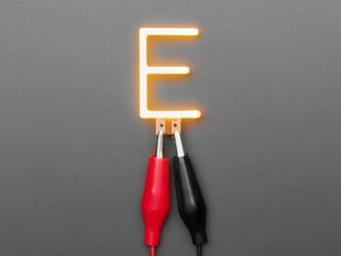 Overhead shot of LED filament in the shape of the letter "E" lit up with alligator clips.