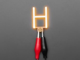 Overhead shot of LED filament in shape of letter "H" lit up with alligator clips.