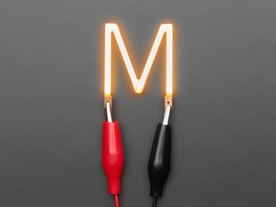 Overhead shot of LED filament in shape of letter "M" lit up with alligator clips.