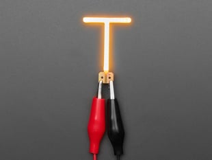 Overhead shot of LED filament in shape of letter T" lit up with alligator clips.