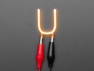 Overhead shot of LED filament in shape of letter "U" lit up with alligator clips.