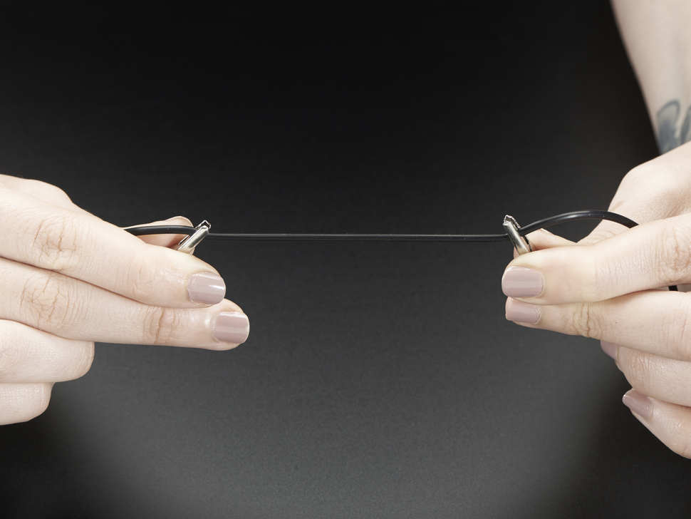 Two hands holding a black rubber cord with two alligator clips.  