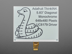 Overhead shot of 5.83" monochrome electronic ink display. Graphic features a friendly python and text: "Adafruit ThinkINK 5.83" Diagonal Monochrome 648x480 Pixels UC8179 Driver."