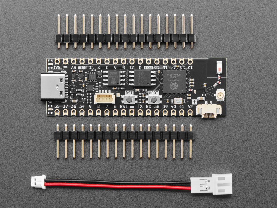 Overhead shot of long, black, skinny, dev board with two pieces of header and a JST-PH adapter cable.