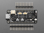 Overhead shot of black, rectangular, Feather microcontroller between two pieces of header.