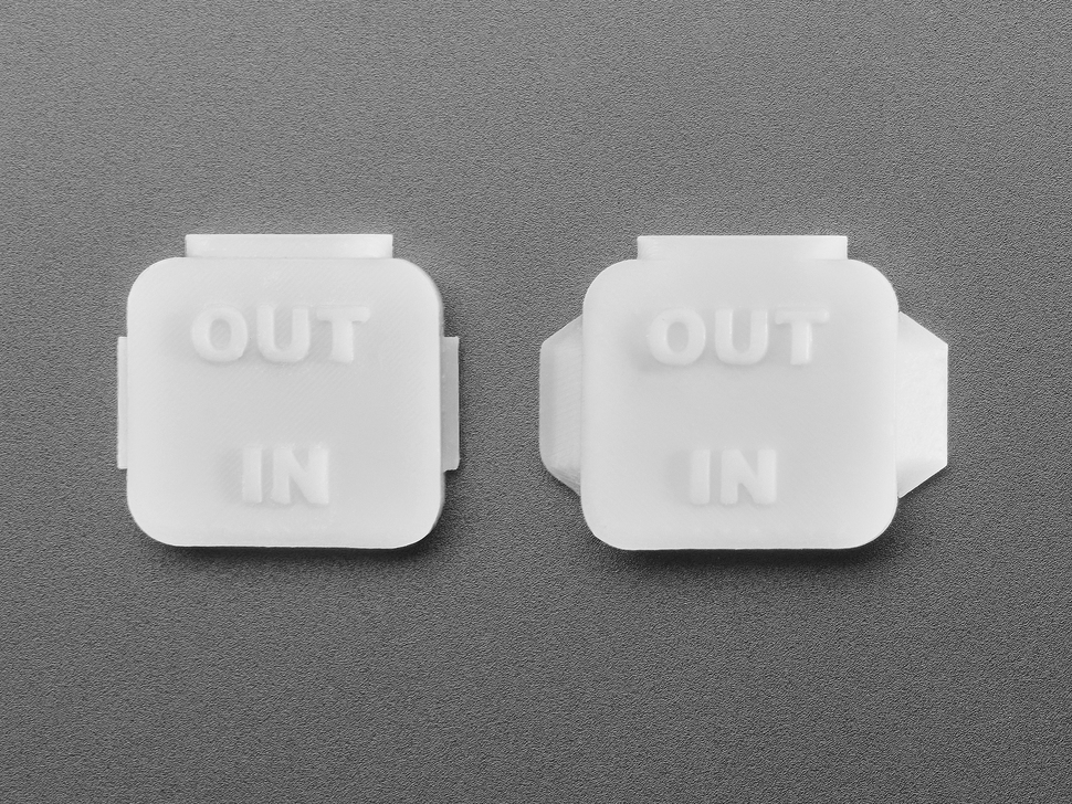 Overhead shot of two pieces of white plastic square-shaped enclosure pieces.