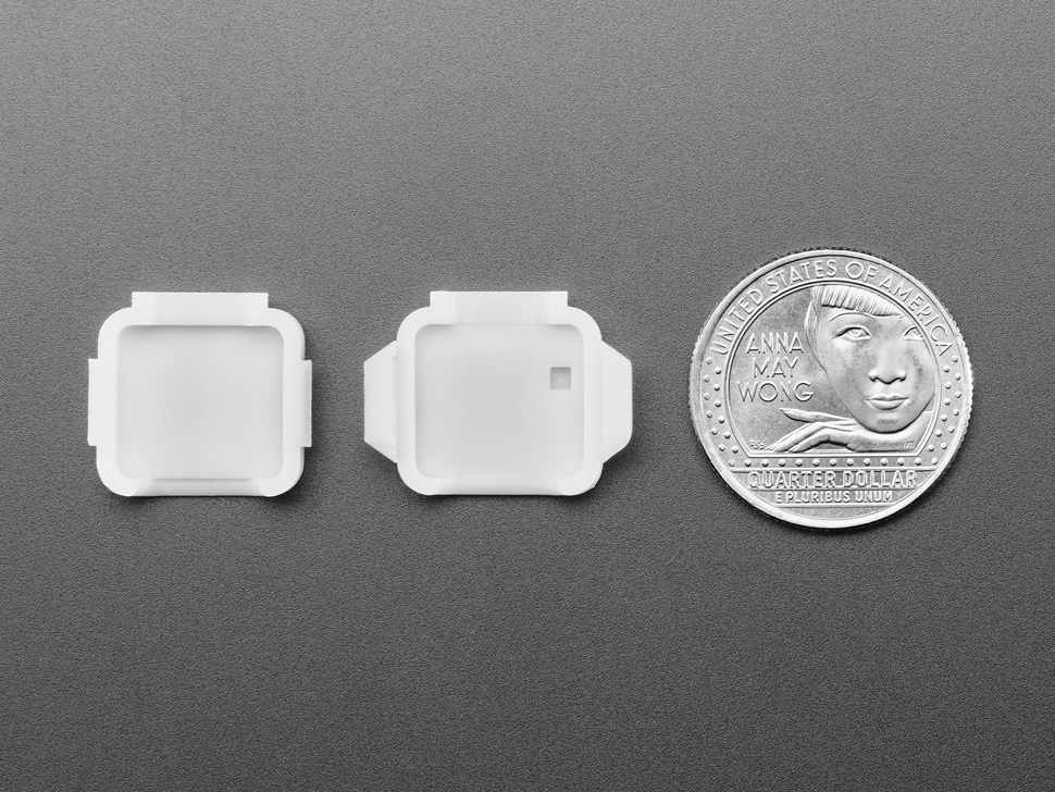 Two pieces of white plastic square-shaped enclosure pieces with U.S. quarter for scale.
