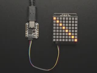 Top-down video of an 8x8 LED matrix wired up to a small, square-shaped microcontroller. The LED matrix displays scrolling text and emoticon faces.
